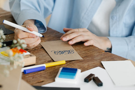 Woman wearing blue shirt sat at a wooden desk writing a Father's Day card