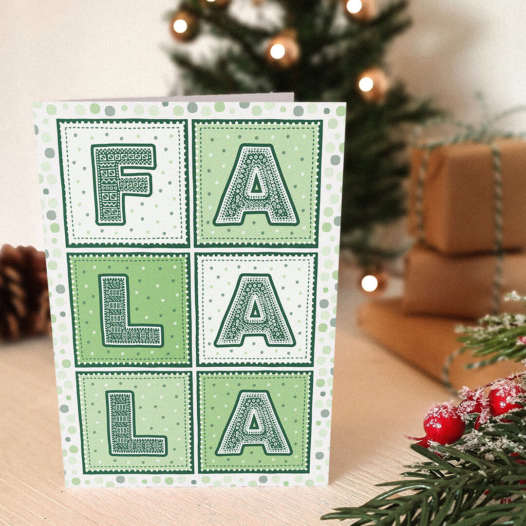 Green Christmas card with 'FA LA LA' typography in front of a decorated Christmas tree and presents.