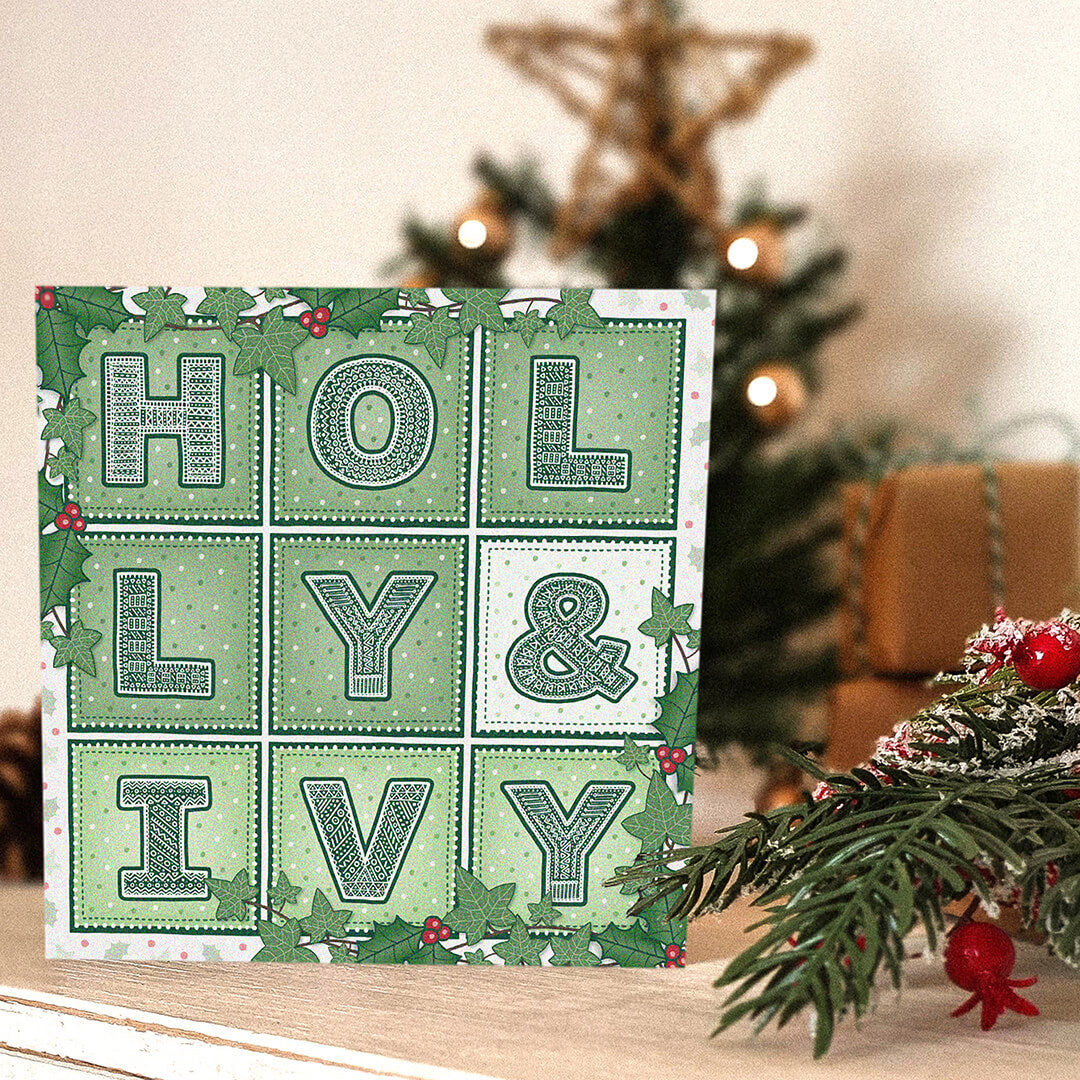 Holly & Ivy Christmas card with 'Holly & Ivy' typography and illustrations in front of a decorated Christmas tree.