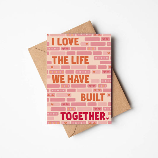 cute pink and orange anniversary card featuring illustrated bricks and i love the life we have built together message blank inside recycled kraft brown envelope