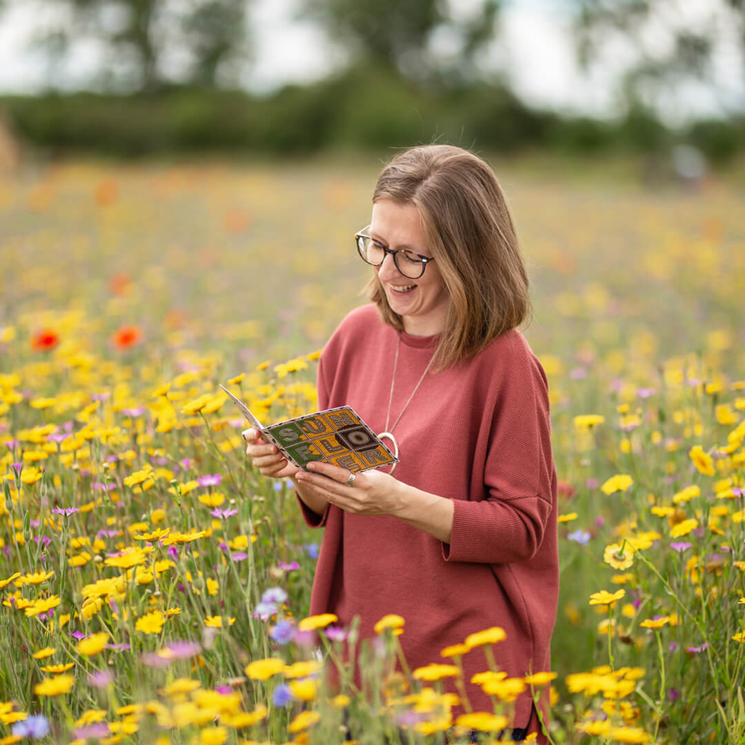 Jess holding a sunflower greeting card stood in a field of yellow flowers
