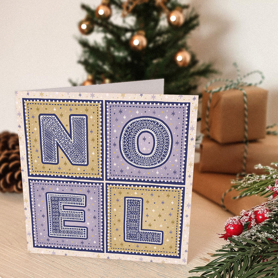 Purple and gold Noel Christmas card with 'NOEL' text in front of a decorated Christmas tree and presents.
