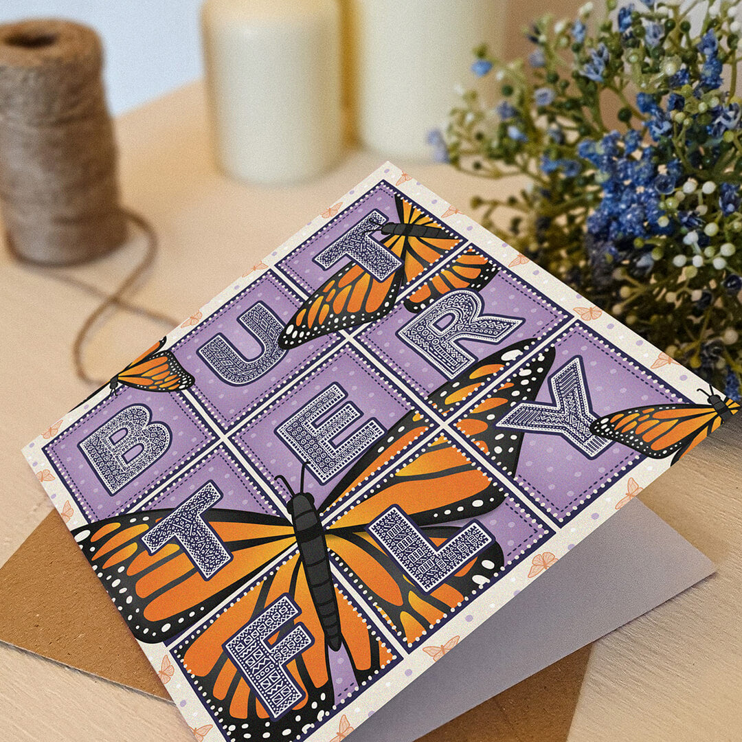 Butterfly greeting card with monarch butterfly illustrations sat on a white wooden dresser with kraft brown recycled envelope and blue flowers.