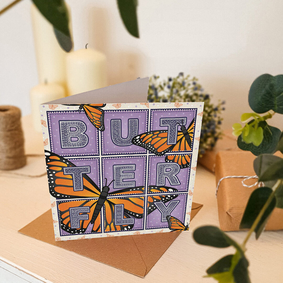 Butterfly greeting card with monarch butterfly illustrations sat on a white wooden dresser with plants and candles in the background.