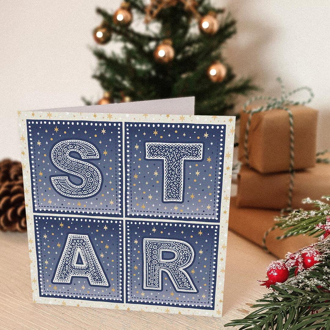 Star Christmas card with 'STAR' typography and star illustrations in front of a decorated Christmas tree and presents.