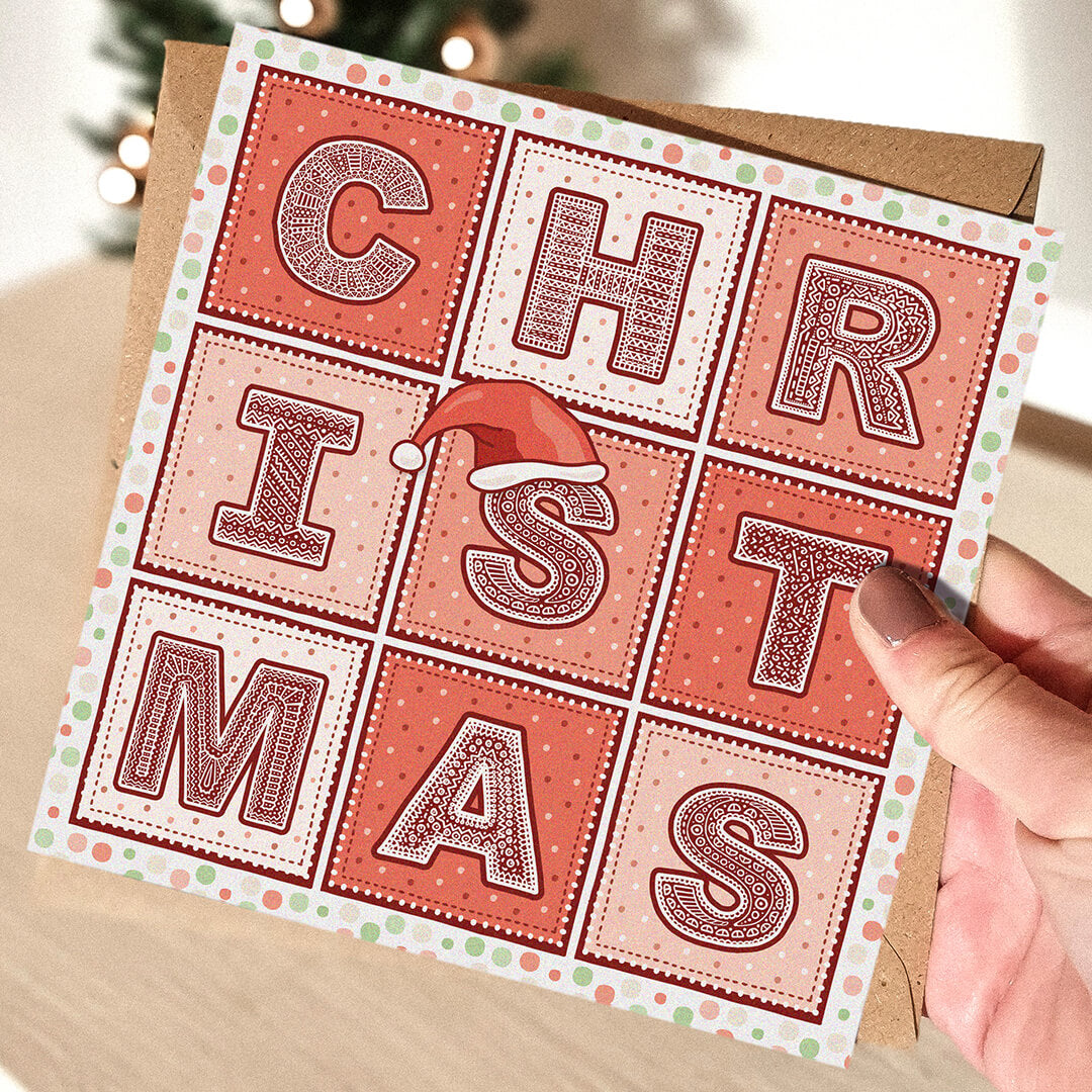 Red Christmas card with 'Christmas' text and a Santa hat illustration held by a hand.
