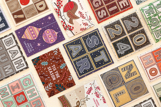 Selection of bright colourful unique Christmas cards laid out flat on a cream wooden surface