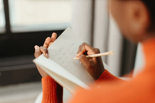 Person wearing bright orange jumper writes a greeting card