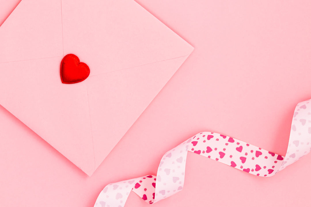 pink envelope and white ribbon with pink hearts sat on a pink background