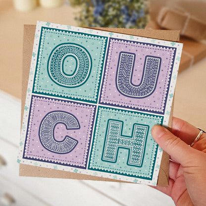 Hand holding purple and turquoise get well soon card Unique ouch colourful get well soon card for friends Printed on FSC-certified card with a kraft brown recycled envelope Blank inside