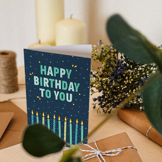 blue and green candles birthday card on shelf with envelope and gift