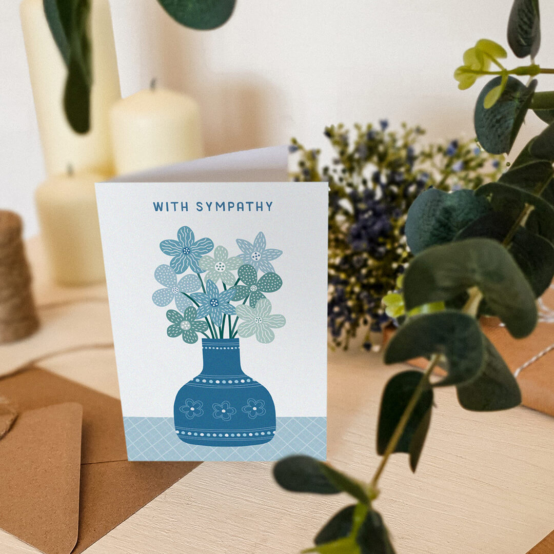 blue floral with sympathy card sat on wooden dresser with plants and candles