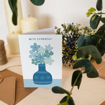 blue floral with sympathy card sat on wooden dresser with plants and candles