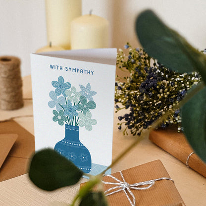 blue floral with sympathy card sat on dresser surrounded by plants, gifts and candles