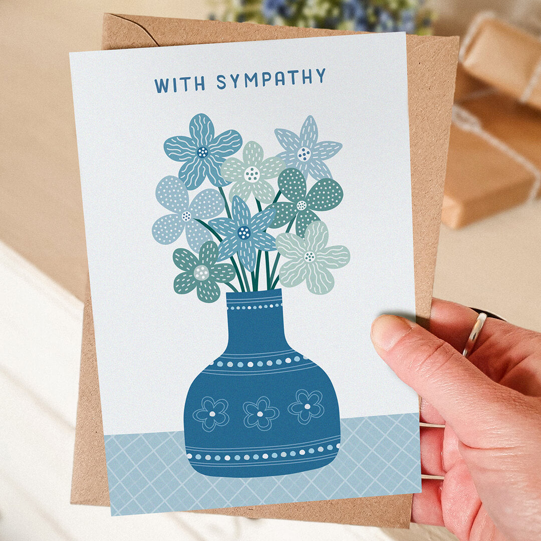 hand holding blue floral with sympathy card with blurred background