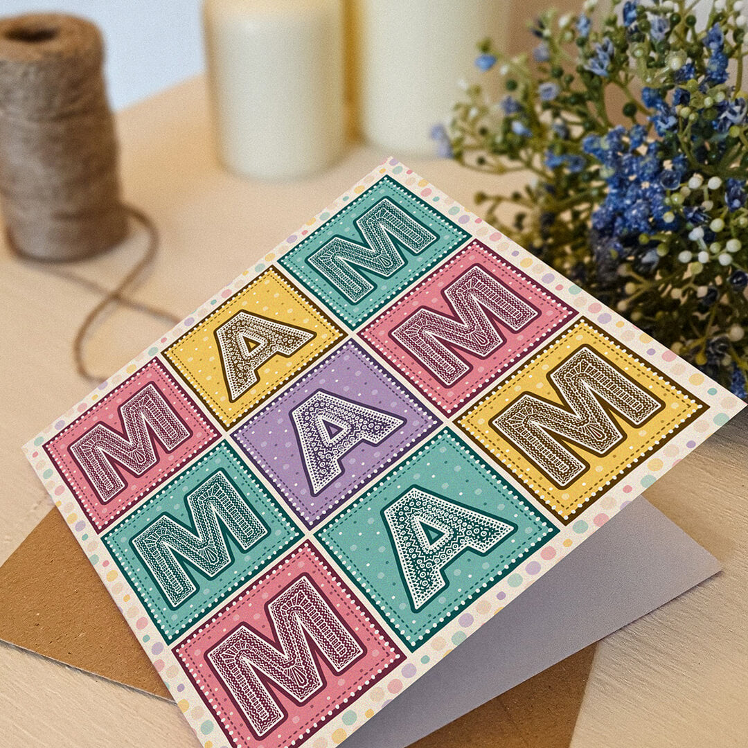 Colourful Mother's Day card with 'MAM' message on a cream wooden table with decorative elements.