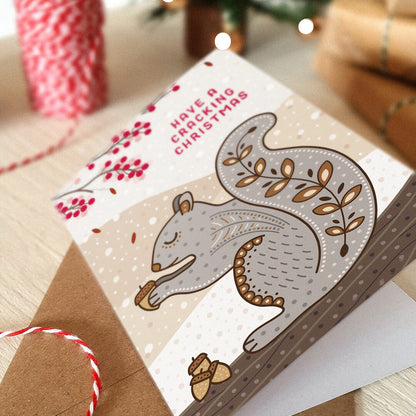 grey squirrel christmas card lying on a tabletop with blurred festive background.