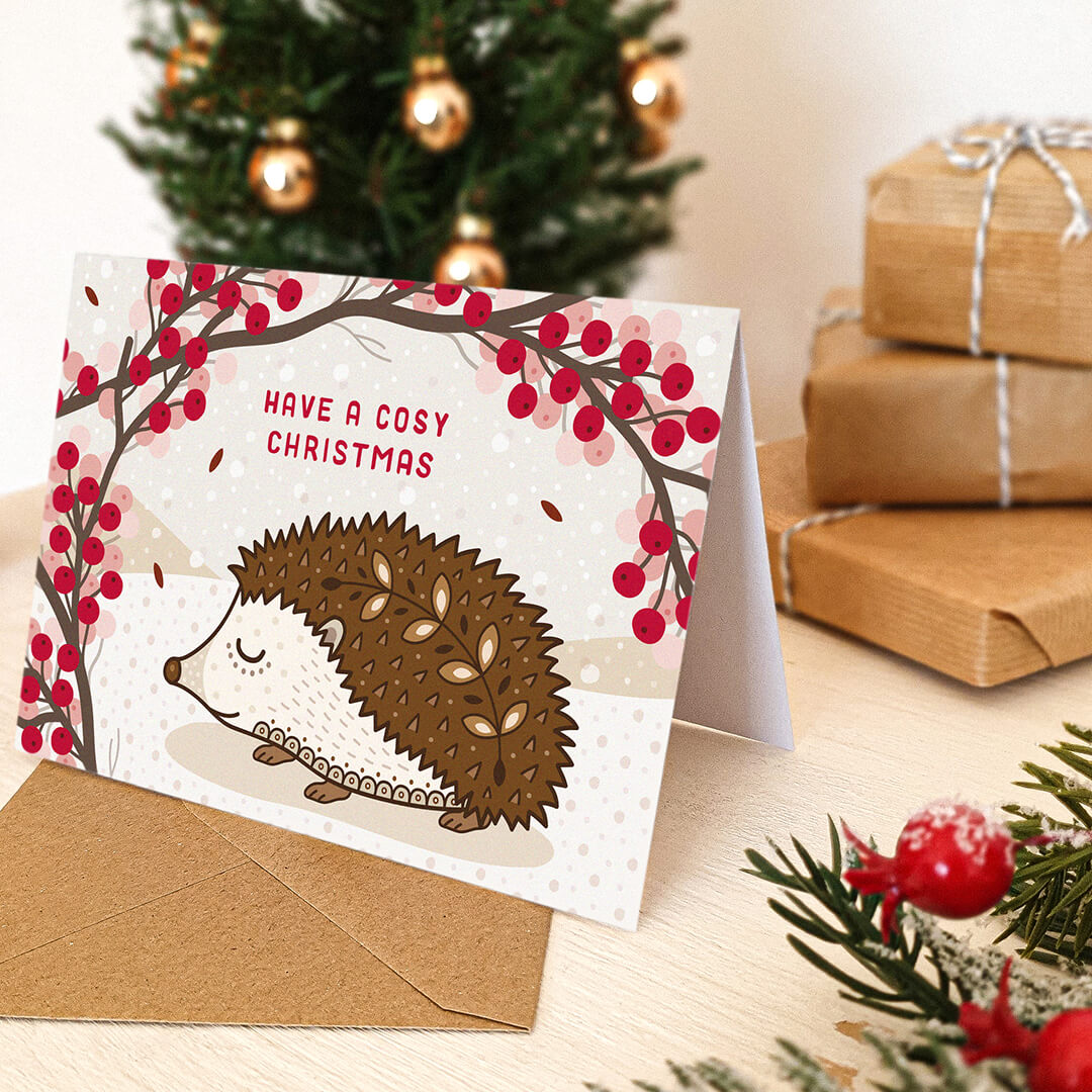 Christmas card with hedgehog design and 'Have a Cosy Christmas' message, surrounded by festive decor.
