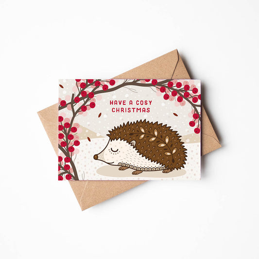 Illustrated Christmas card with a hedgehog and berries, featuring a kraft brown envelope on a white background.