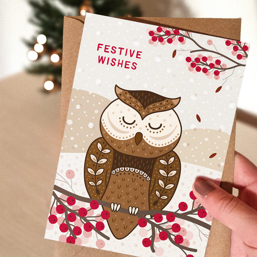 Christmas card with an owl design and 'Festive Wishes' message, held by a hand.