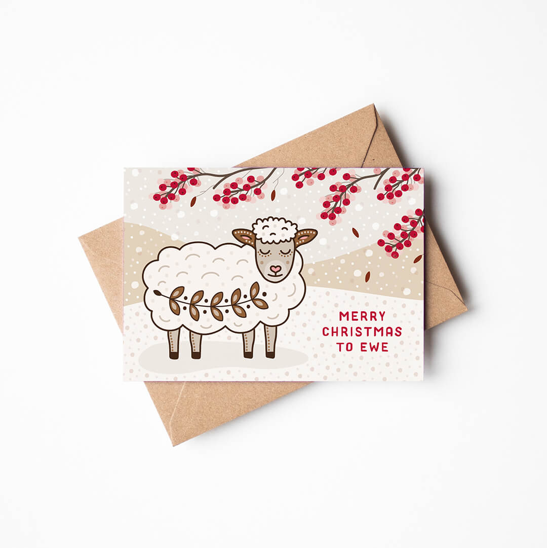 a christmas card with cute sheep design with kraft brown envelope sat on a white background