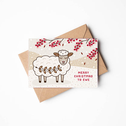 a christmas card with cute sheep design with kraft brown envelope sat on a white background