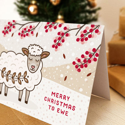 A cute sheep christmas card on a tabletop with blurred christmas tree and gifts in the background