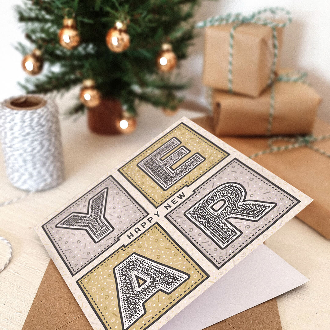 New Year's card with decorative text on a cream wooden table with Christmas decorations in the background
