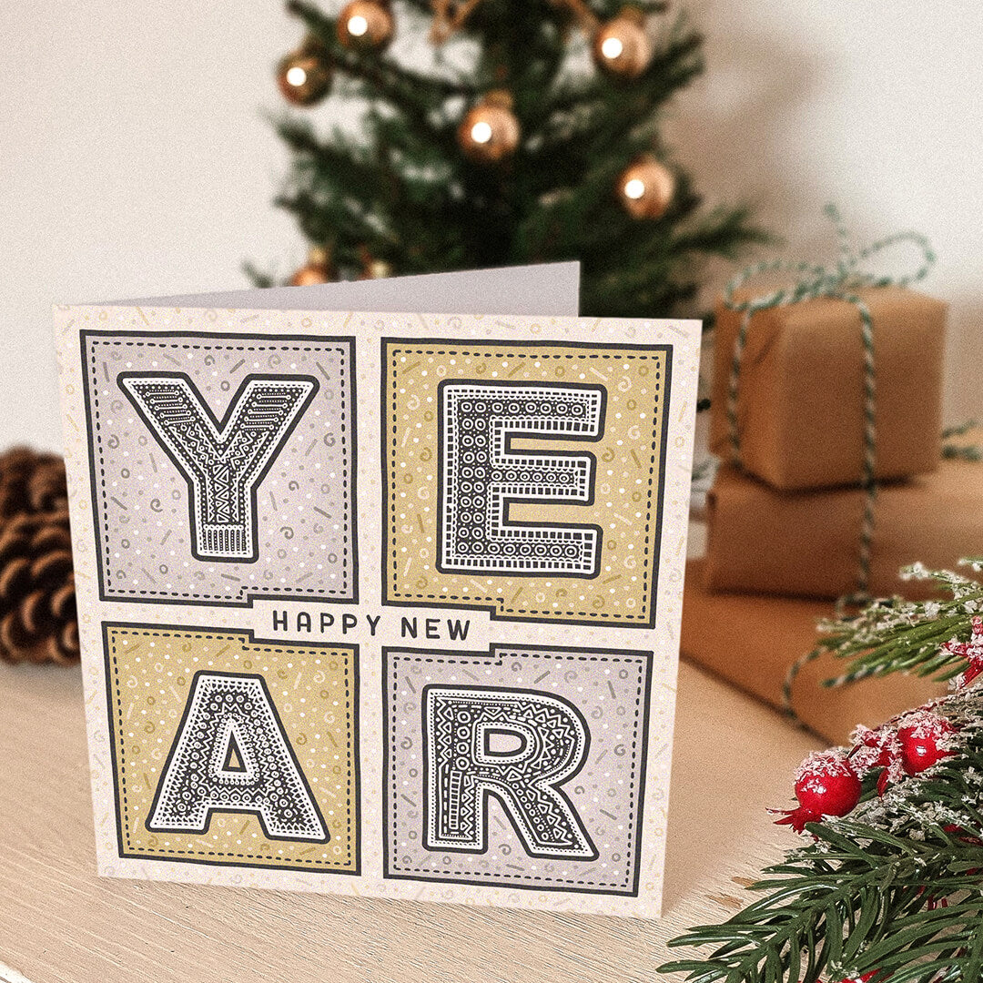 Unique New Year's card with decorative text in front of a Christmas tree and gifts.