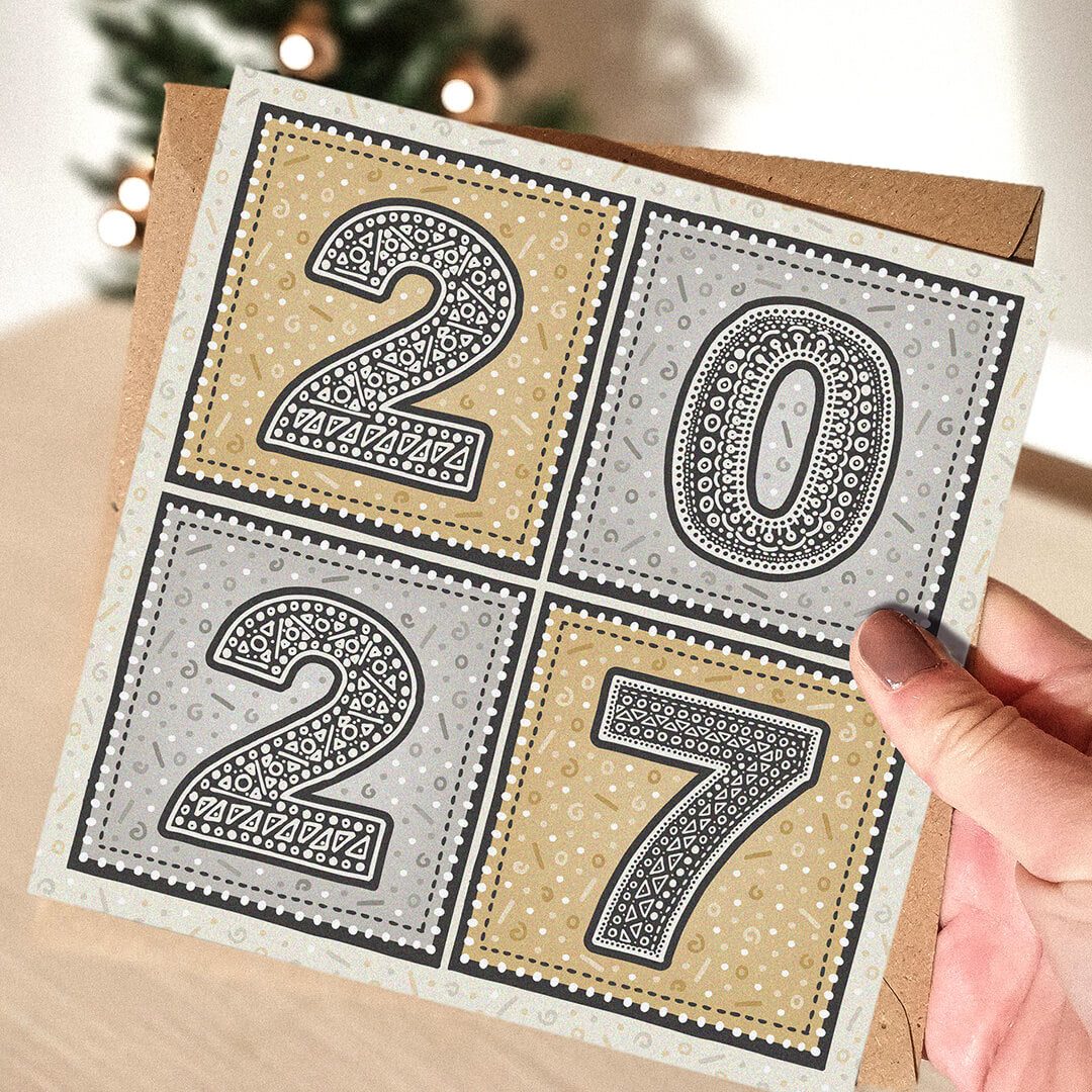 hand holding unique gold and silver 2027 new year card with blurred christmas tree in the background
