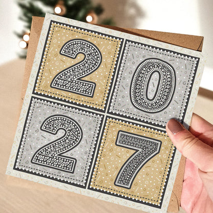 hand holding unique gold and silver 2027 new year card with blurred christmas tree in the background