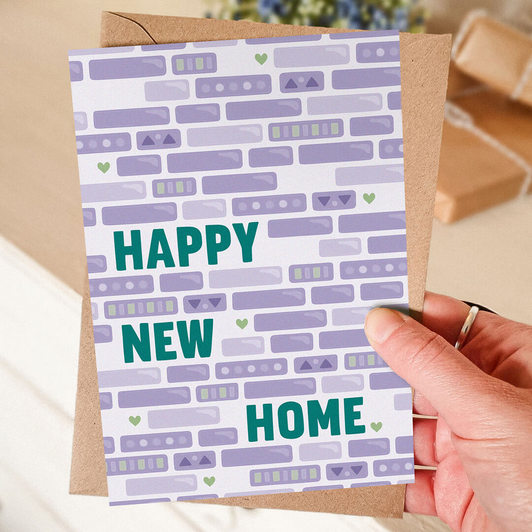 hand holding green and purple happy new home card featuring brick illustrations blank inside recycled kraft brown envelope