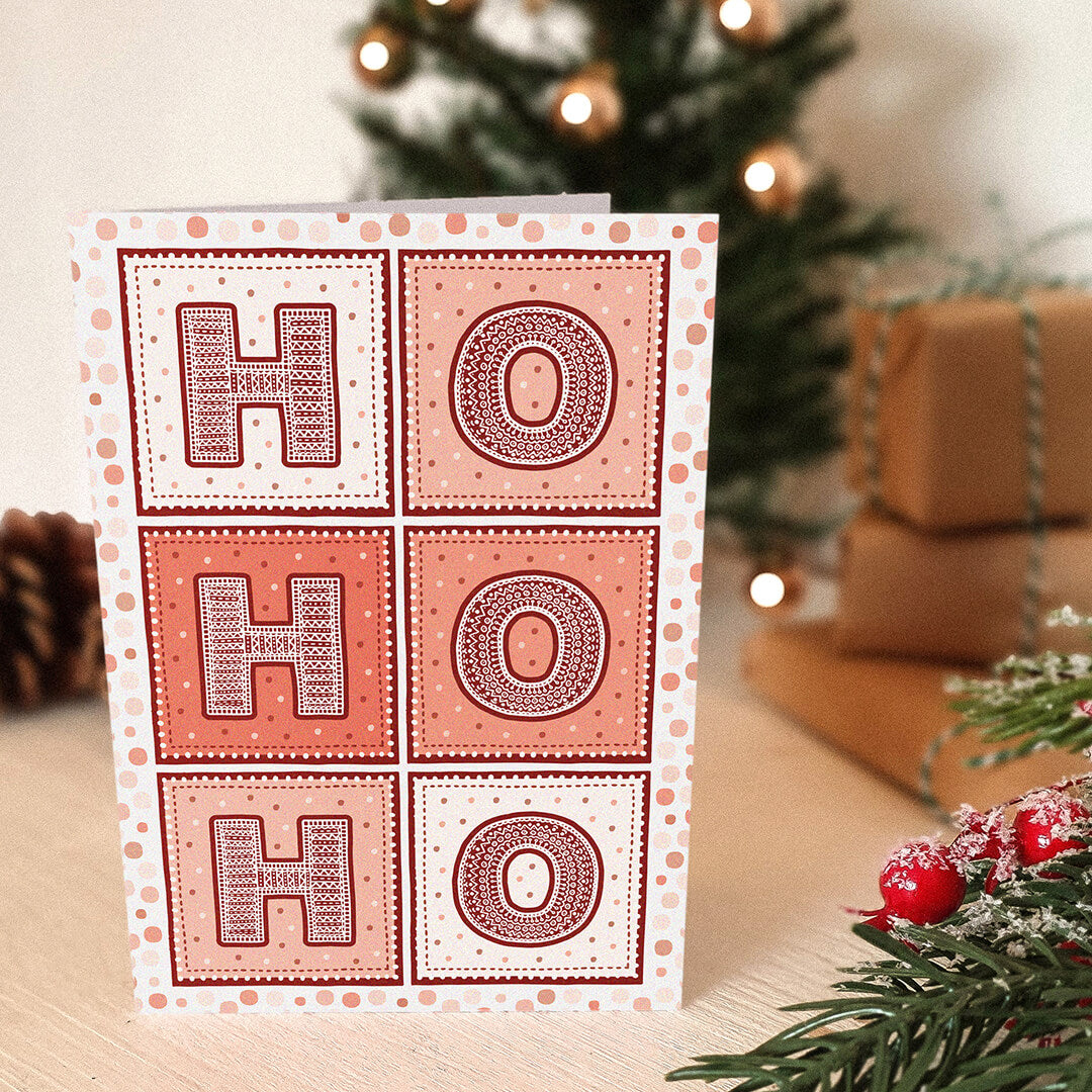 Red Ho Ho Ho Christmas card with 'HO HO HO' text, with a blurred Christmas tree and presents in the background.