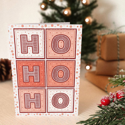 Red Ho Ho Ho Christmas card with 'HO HO HO' text, with a blurred Christmas tree and presents in the background.