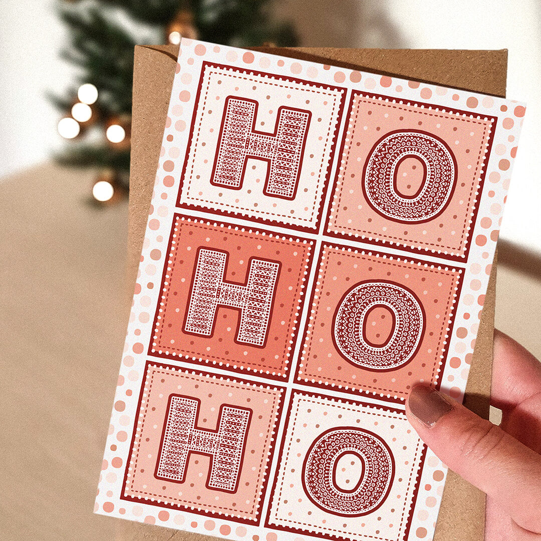 Red Ho Ho Ho Christmas Card with 'HO HO HO' text held by a hand, Christmas tree in the background