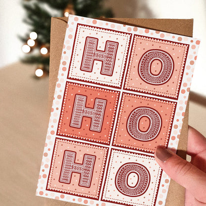 Red Ho Ho Ho Christmas Card with 'HO HO HO' text held by a hand, Christmas tree in the background