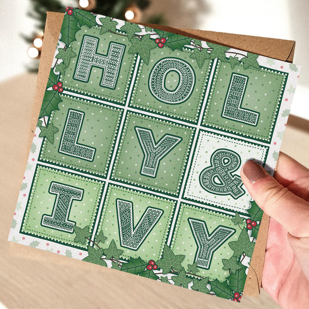 Hand holding a green Christmas card with 'Holly & Ivy' design and illustrations