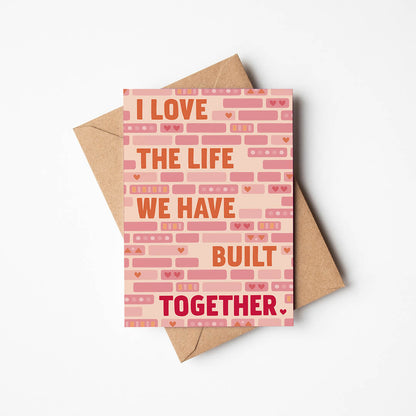 cute pink and orange anniversary card featuring illustrated bricks and i love the life we have built together message blank inside recycled kraft brown envelope