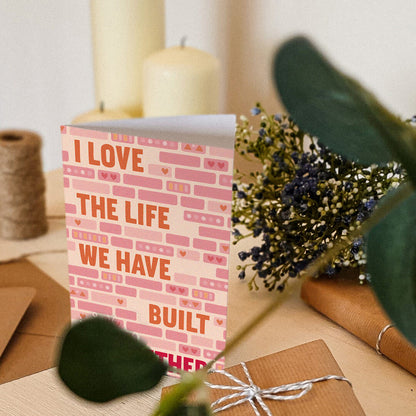 pink and orange anniversary card featuring illustrated bricks and i love the life we have built together message blank inside recycled kraft brown envelope