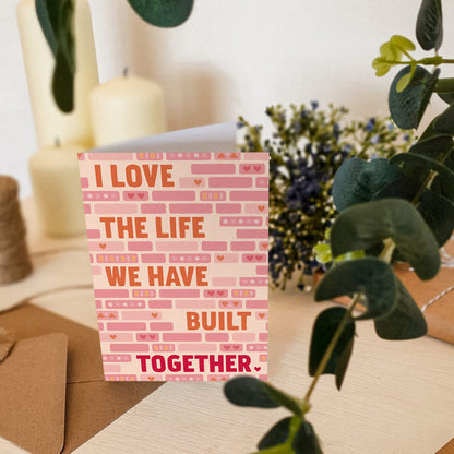 cute pink and orange anniversary card featuring i love the life we have built together message surrounded by illustrated bricks blank inside recycled kraft brown envelope