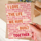 hand holding cute pink and orange valentines day card featuring i love the life we have built together message and brick illustrations blank inside recycled kraft brown envelope