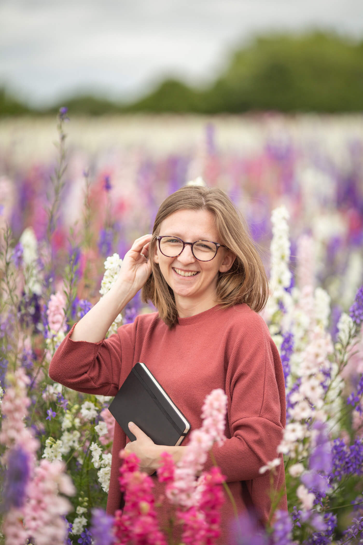 Jess stood in a field of wildflowers holding a black notebook