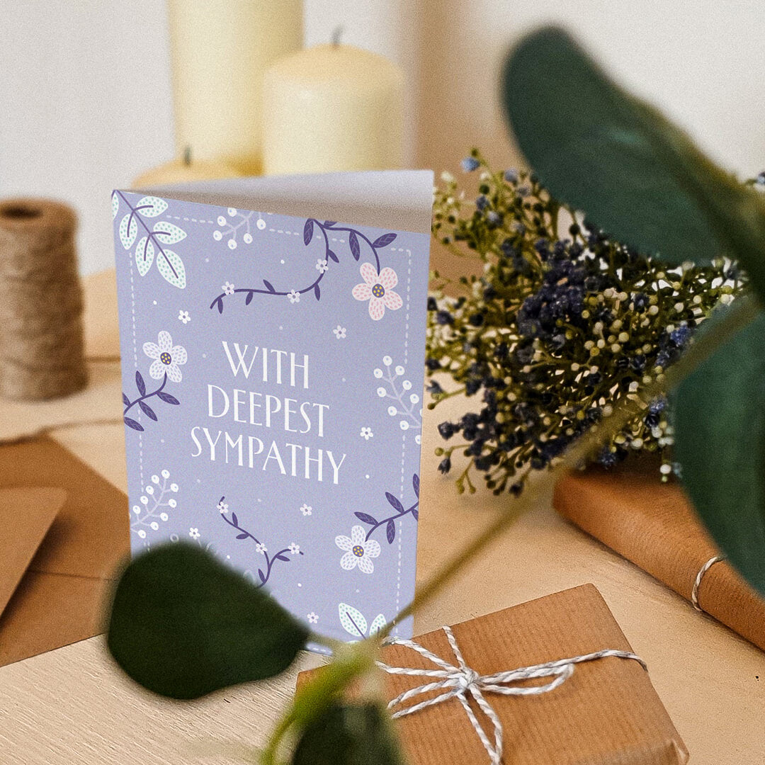 lilac floral sympathy card sat on a dresser surrounded by plants, candles and gifts