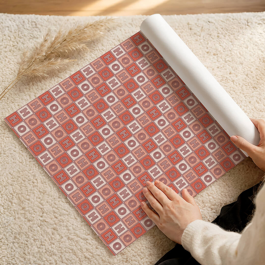 Person unrolling a roll of red Ho Ho Ho Christmas wrapping paper on a fluffy cream rug.