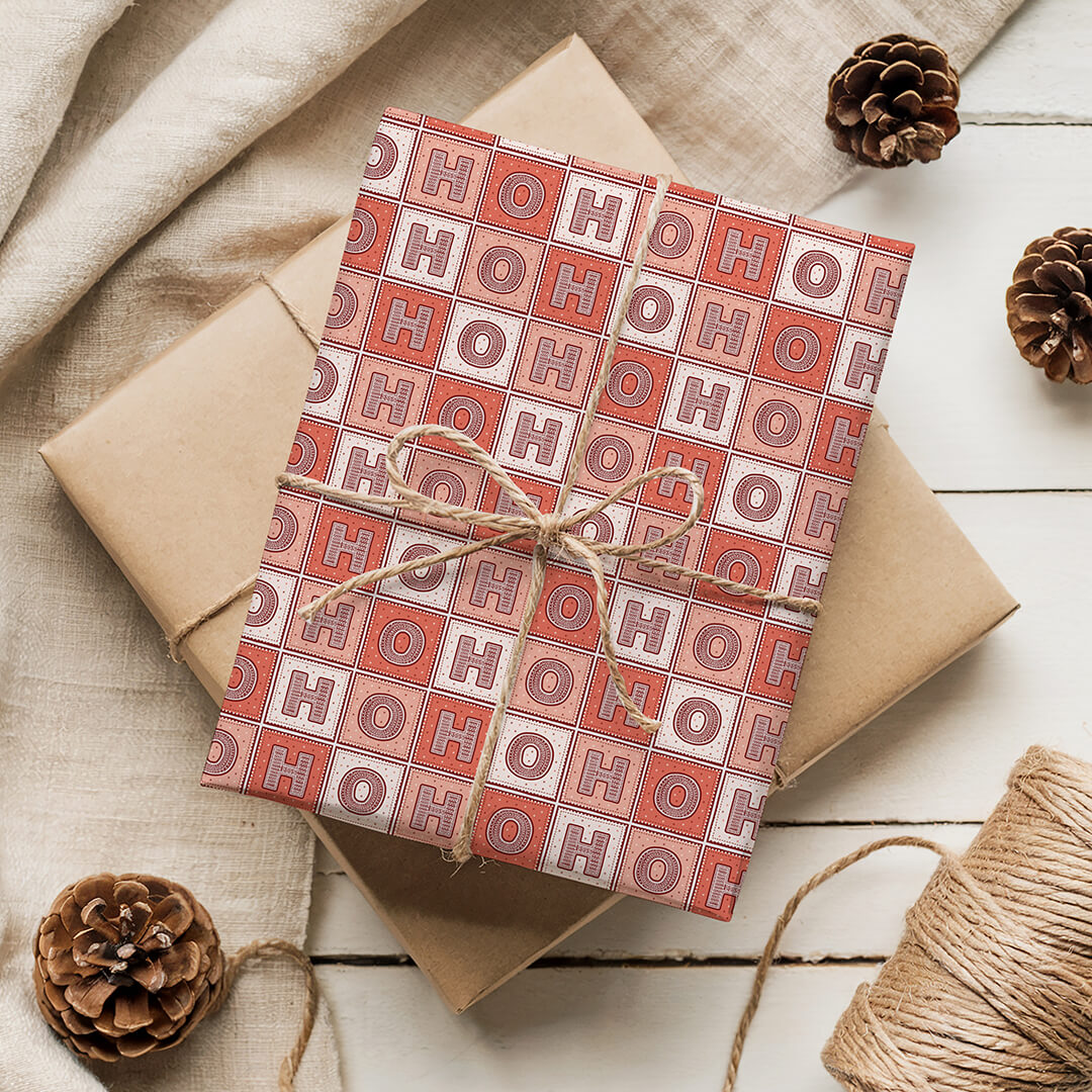 Gift wrapped in 'HO HO HO' patterned Christmas wrapping paper with brown twine on a wooden surface.