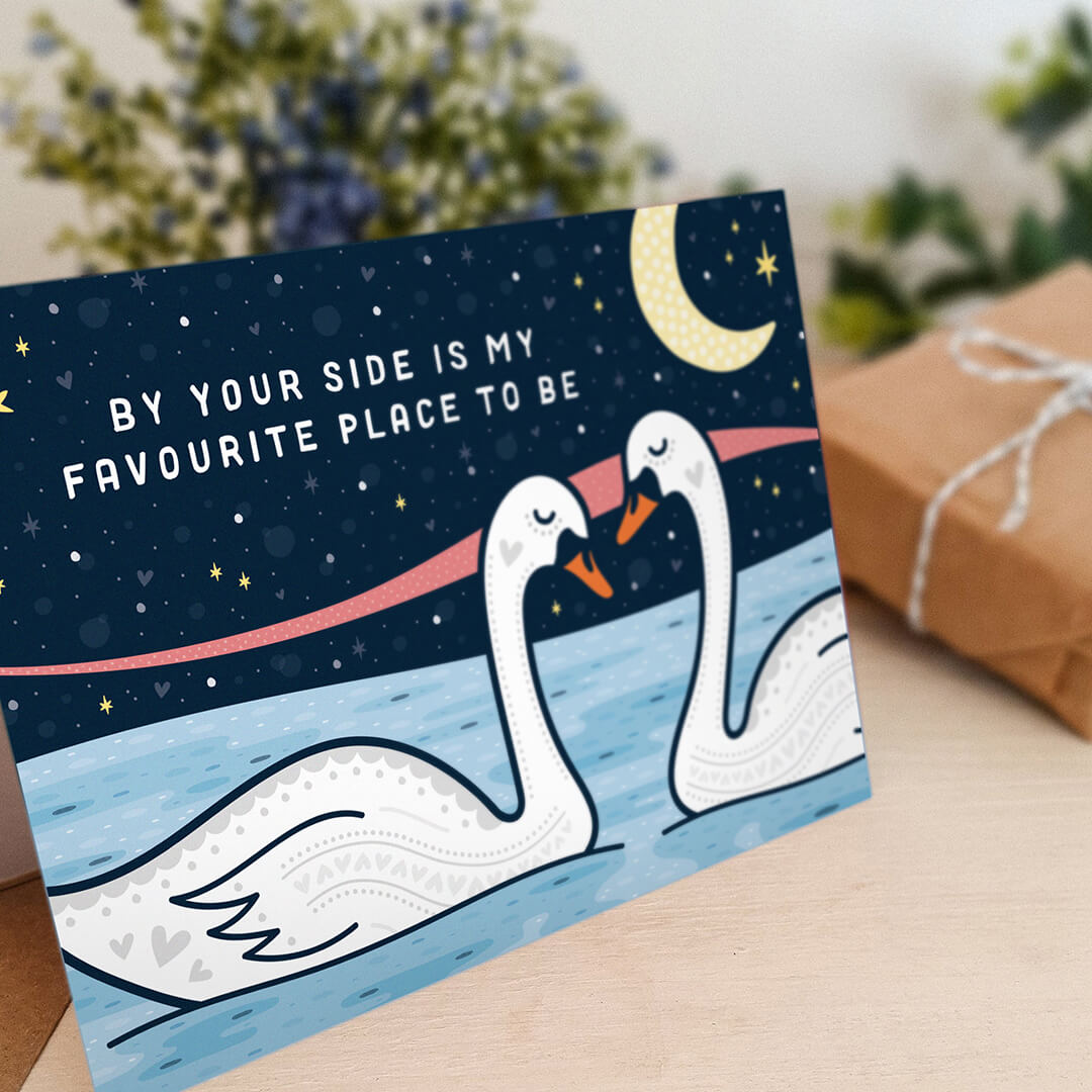 romantic valentines day card featuring two swans under a moonlit night sky and 'by your side is my favourite place to be' message blank inside recycled kraft brown envelope