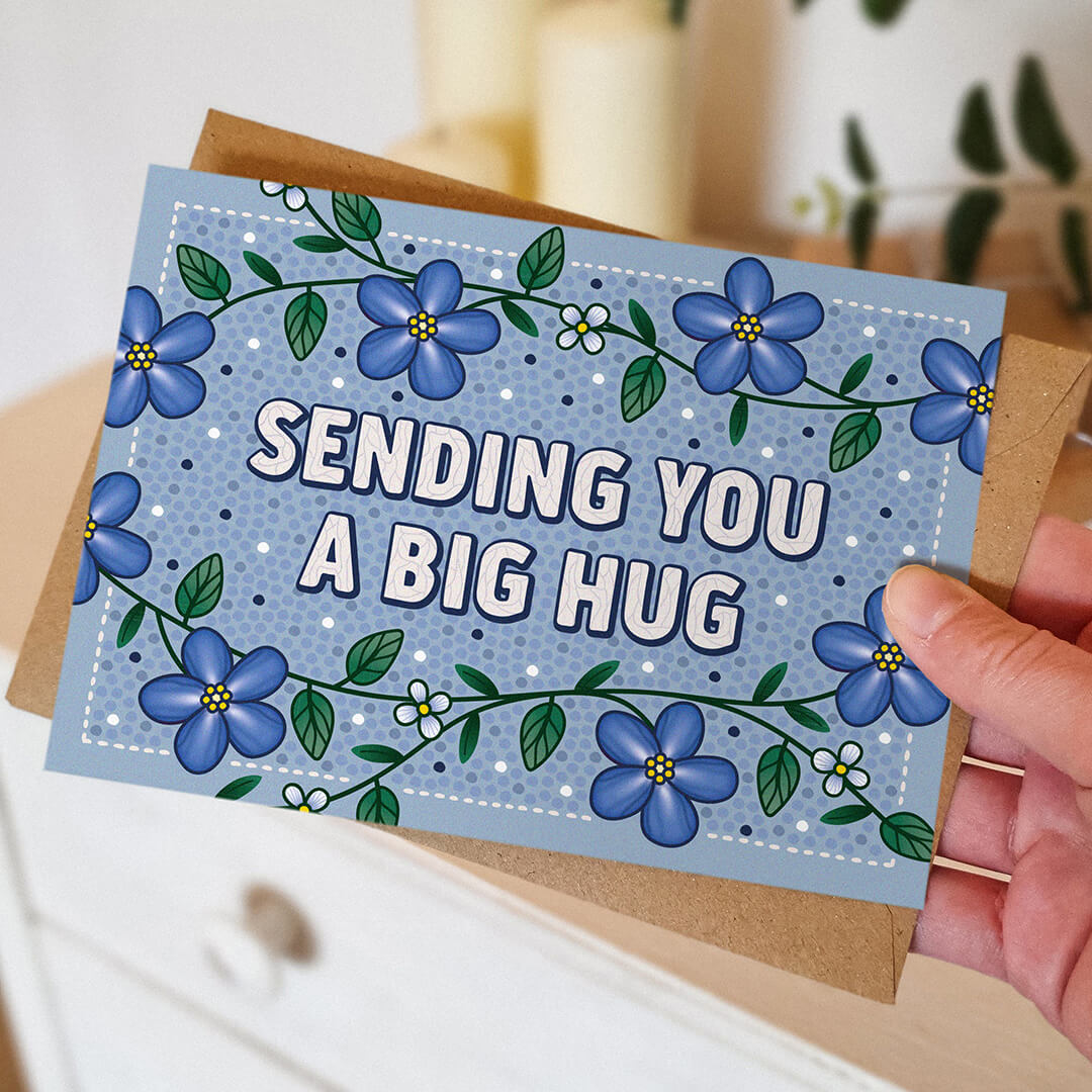 Hand holding blue thinking of you card featuring unique blue floral illustrations Unique sending you a big hug thinking of you card for loved ones Printed on FSC-certified card and supplied with a kraft brown recycled envelope