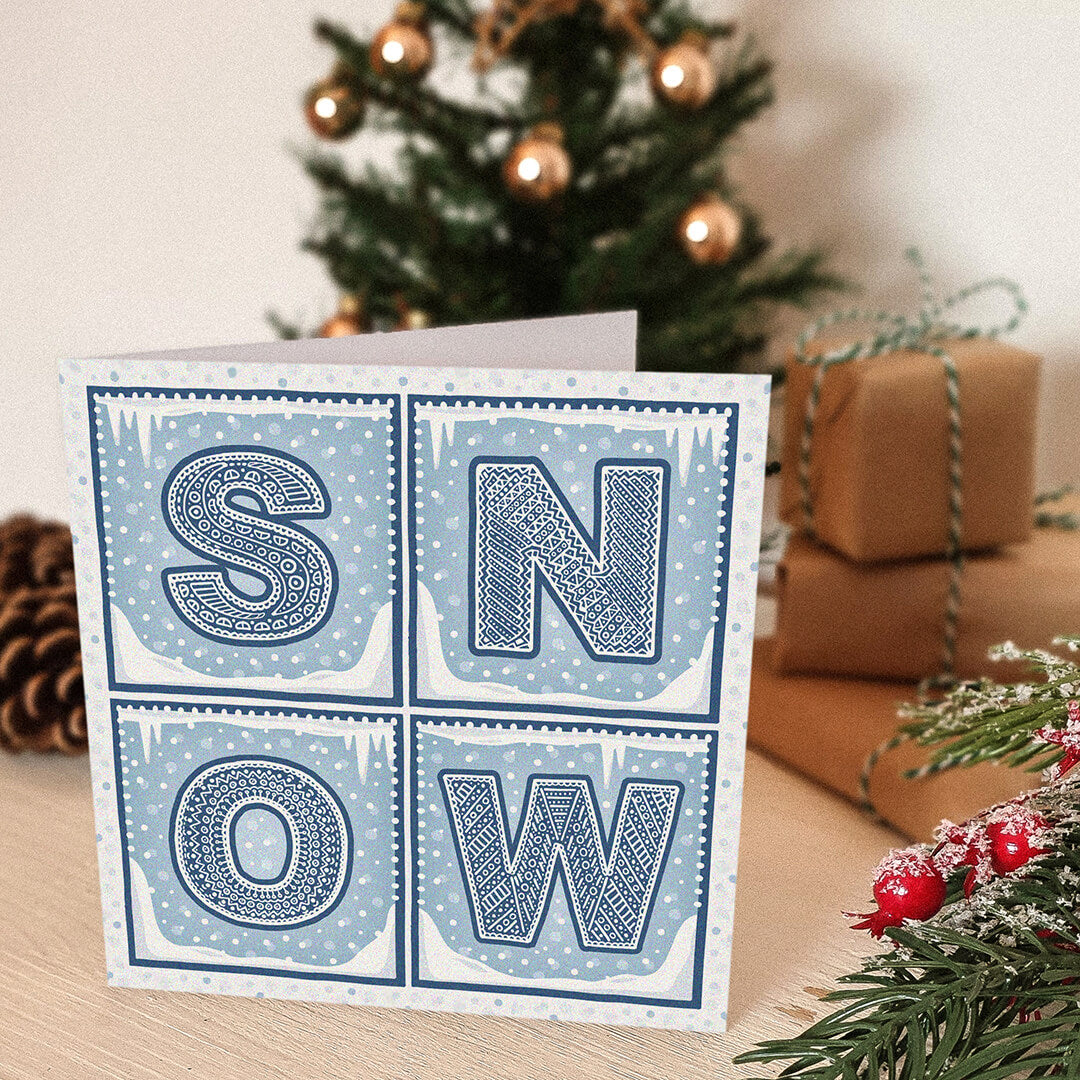 Snow Christmas card with 'SNOW' text and falling snow illustrations in front of a decorated Christmas tree and presents.