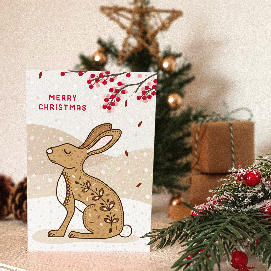 Christmas card with a rabbit or hare illustration and 'Merry Christmas' message, placed in front of a decorated Christmas tree.