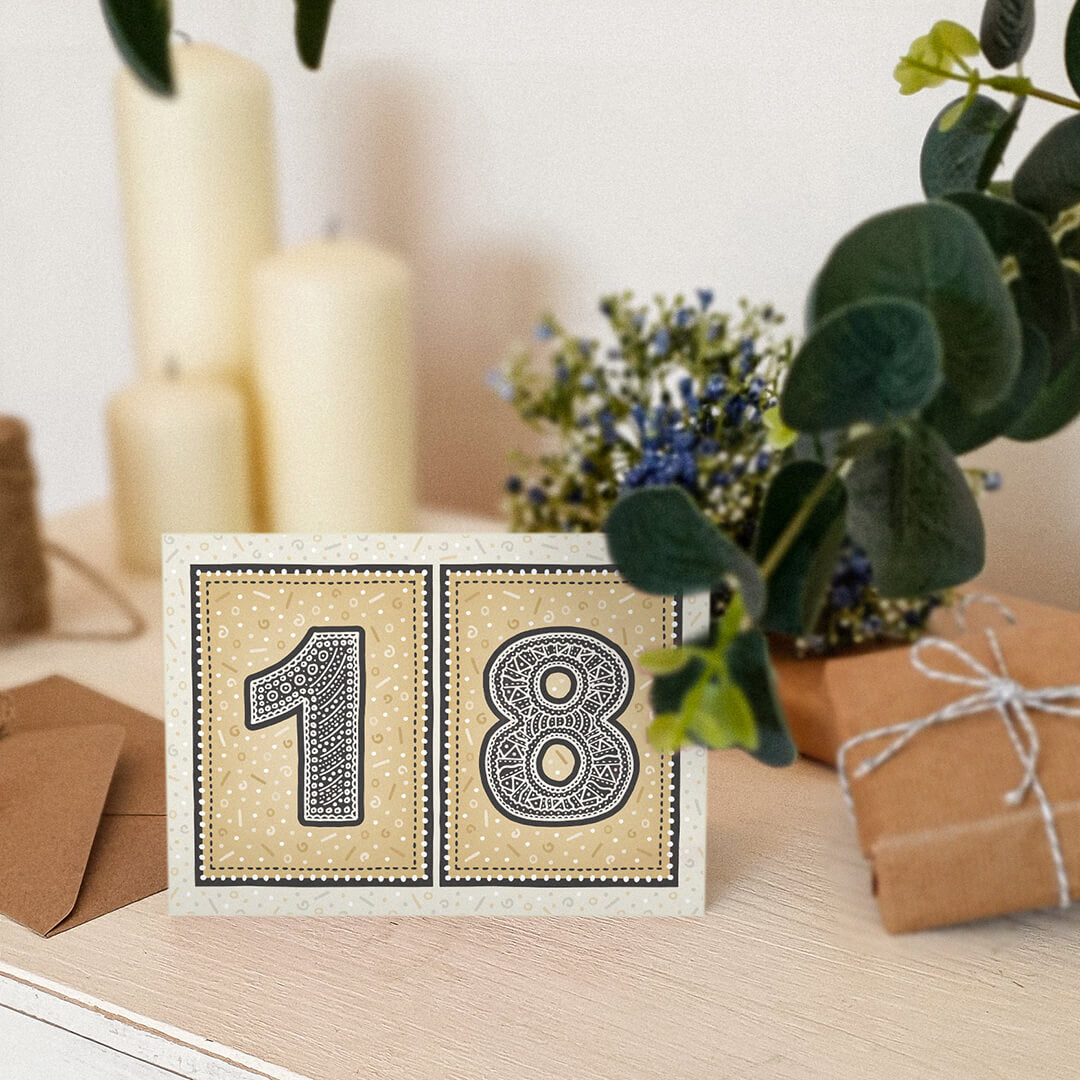 unique black and gold 18th birthday card sat on white wooden dresser with candles and plants